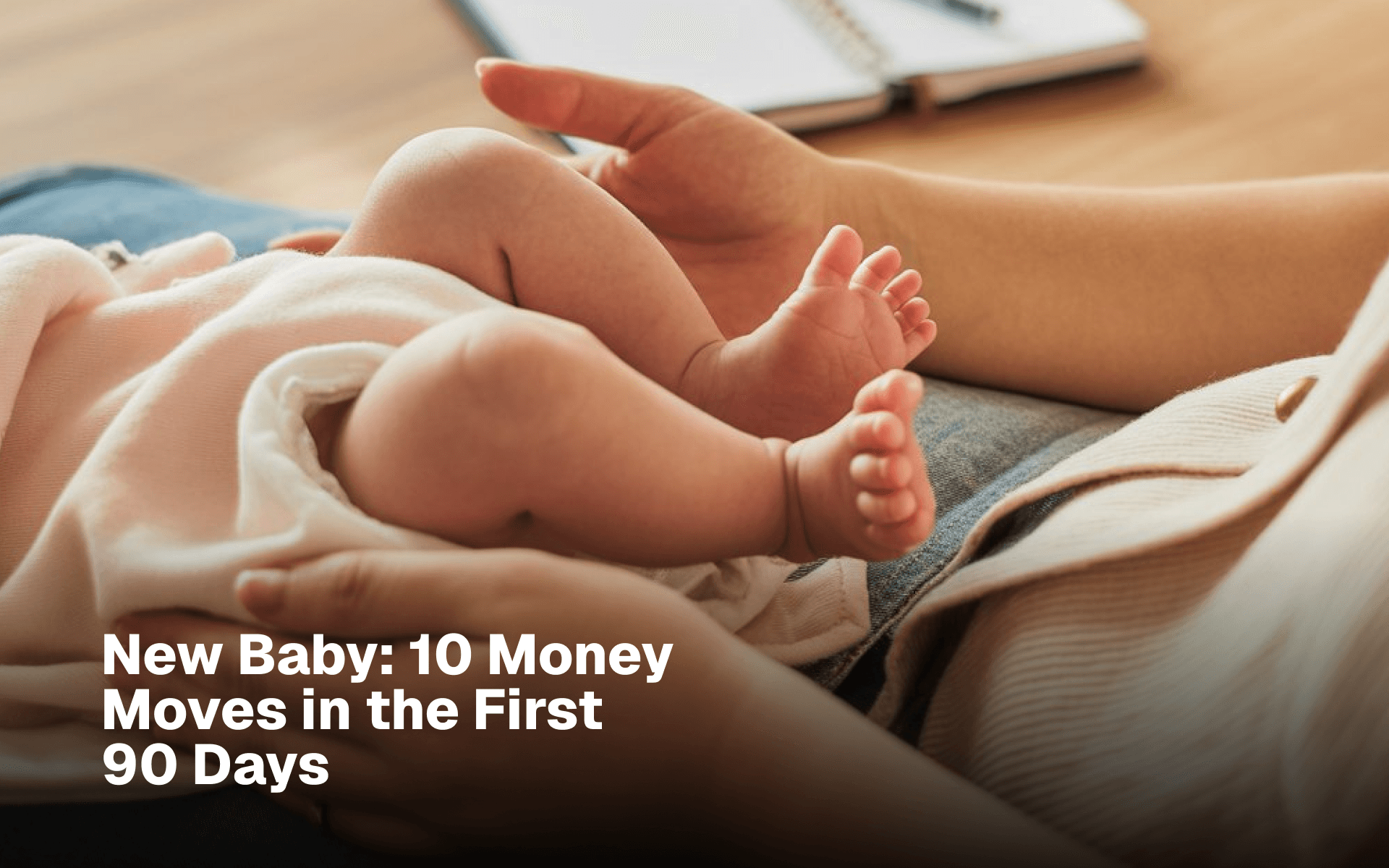 Newborn baby resting on a parent's lap beside a notebook of financial notes