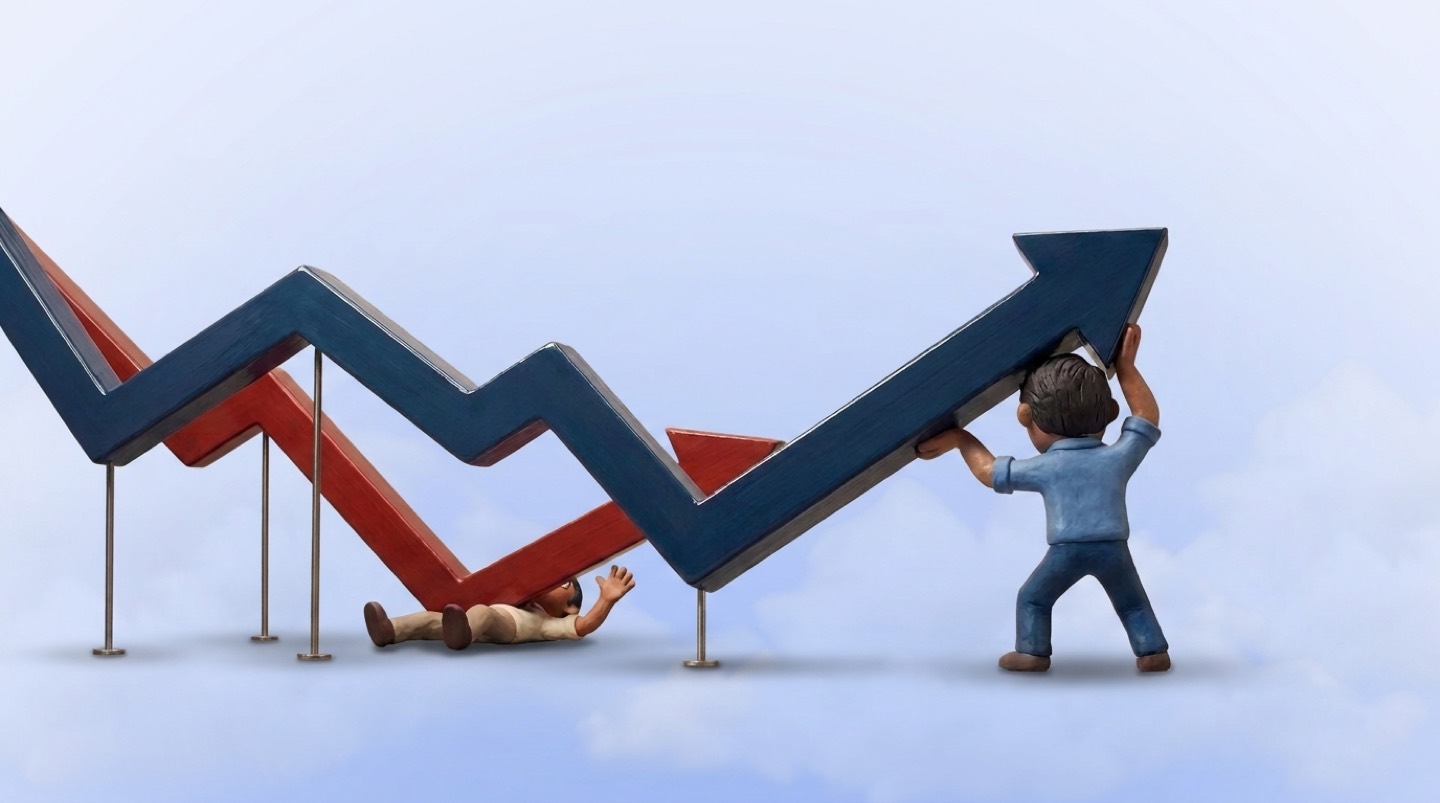Two thick 3D line graphs, one blue and one red, run side by side against a pale blue sky with soft clouds. A clay man seen from behind braces his legs and pushes the blue line up at its arrowhead, while a second clay man lies pinned flat under the red line where it has crashed down, one hand waving.