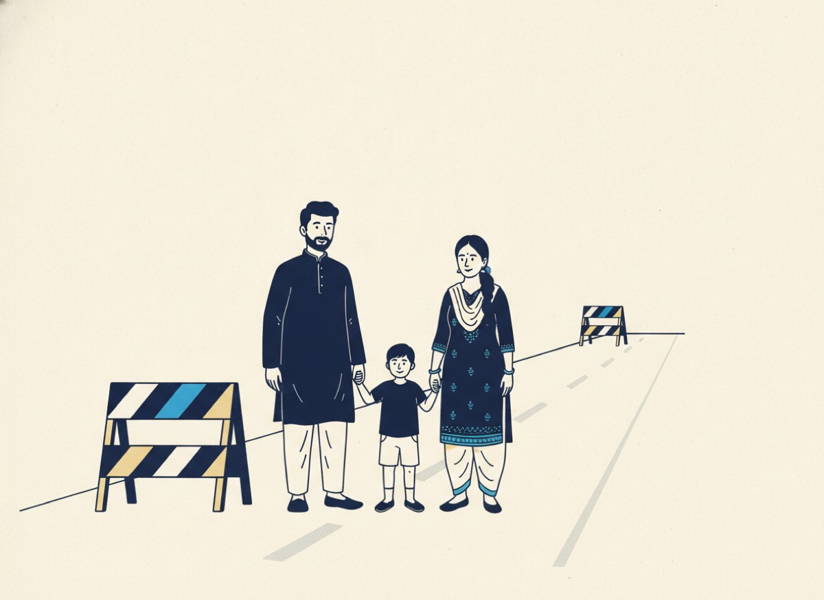 An Indian couple and a young child standing in the middle of an empty road, with a striped barrier beside them and a second identical striped barrier further up the same road